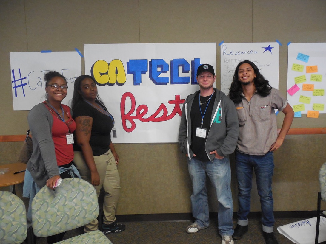 Four people posing in front of handmade signs reading 'CA Tech Fest' at a technology unconference.